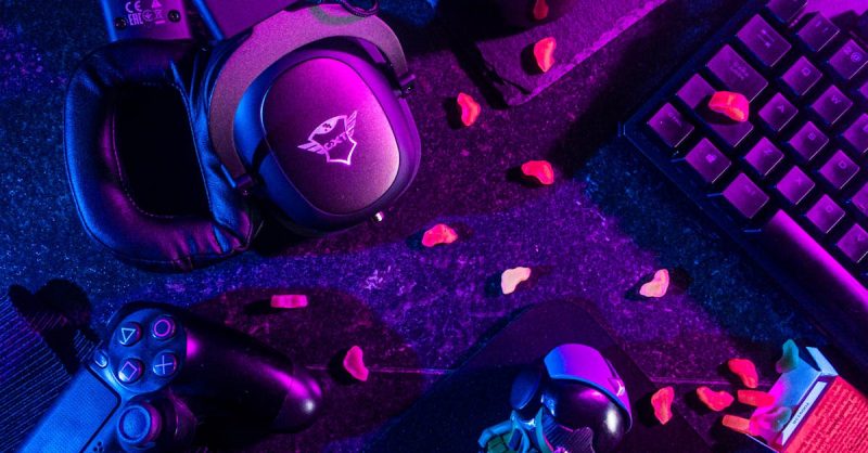pexels-photo-3165335-3165335 Colorful flat lay of gaming gear including headset, controller, and keyboard under vibrant lighting.