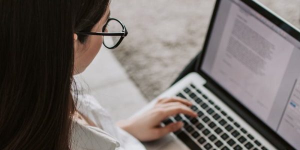 Woman working remotely with a laptop on the floor next to a sofa, enjoying comfortable home office setup.